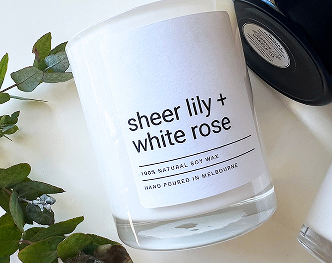 Soy wax candle labeled "sheer lily + white rose," hand poured in Melbourne, surrounded by greenery.